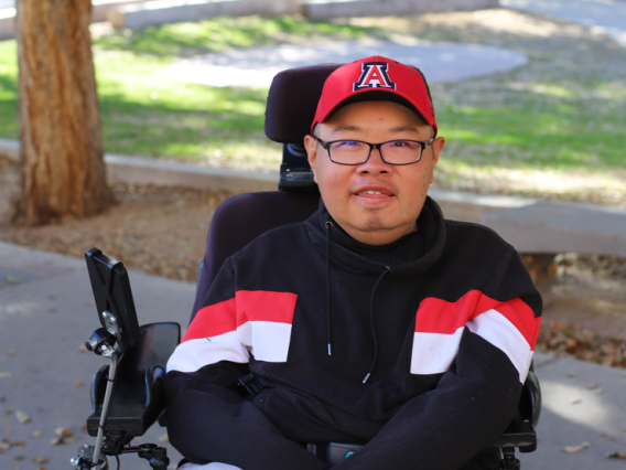 A headshot of Shawn in his wheelchair with greenery in the background